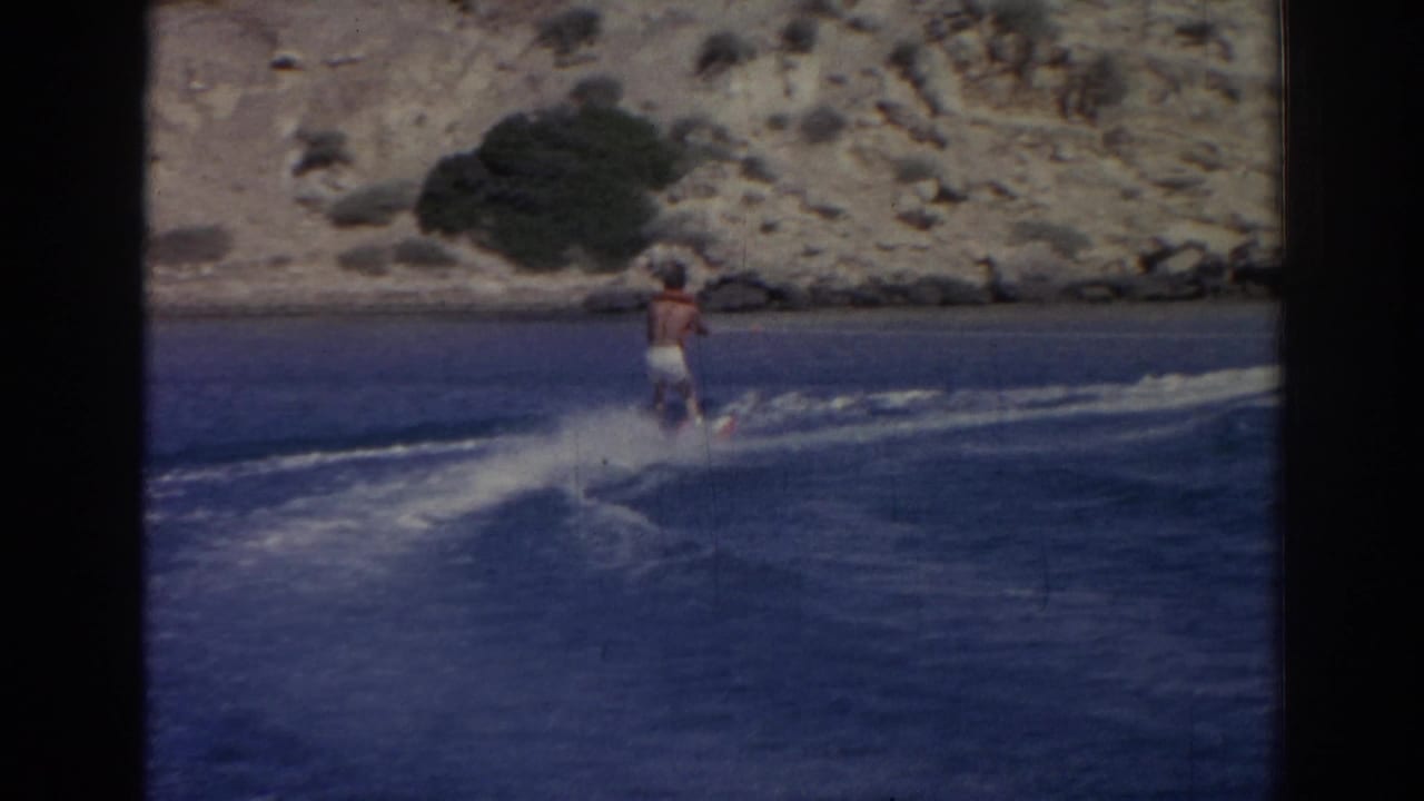 Man pulled across blue water with a rocky shore behind him.