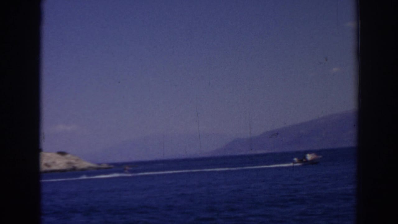 Motorboat traveling across blue water beside rocky shore with hazy land in the distance.