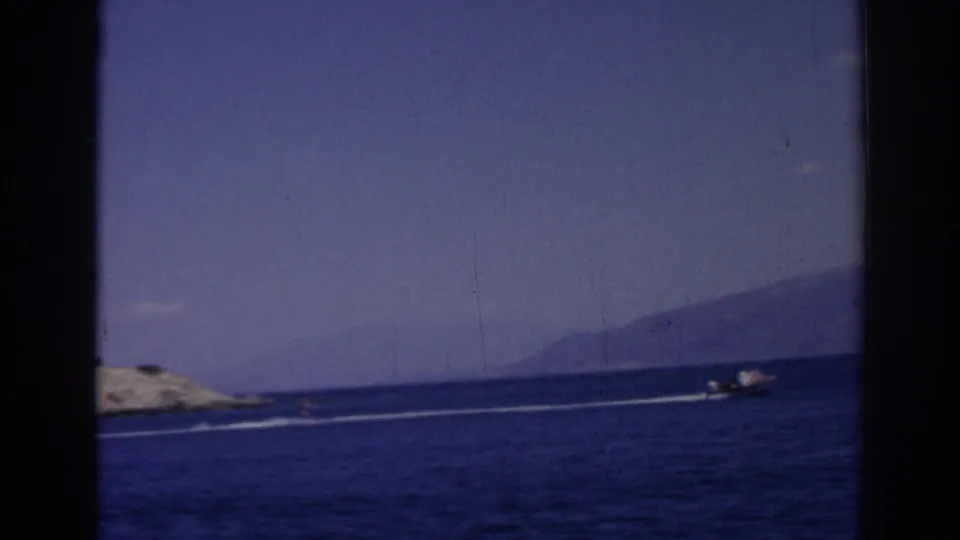 1962 Izmir coastal footage with a small motorboat moving across the blue sea near rocky shore and distant land.