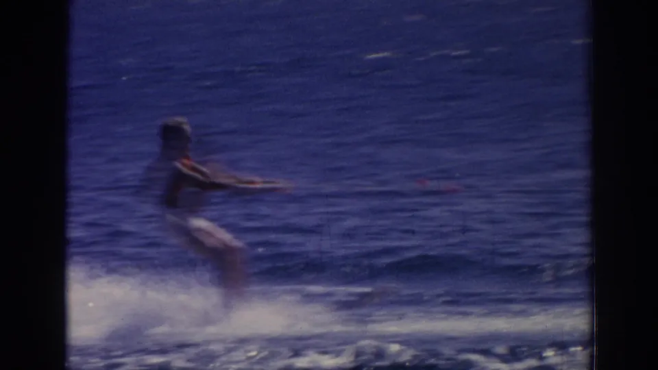 A distant person water skiing in 1962 Izmir, Turkey footage, seen from a handheld 8mm camera over blue water.