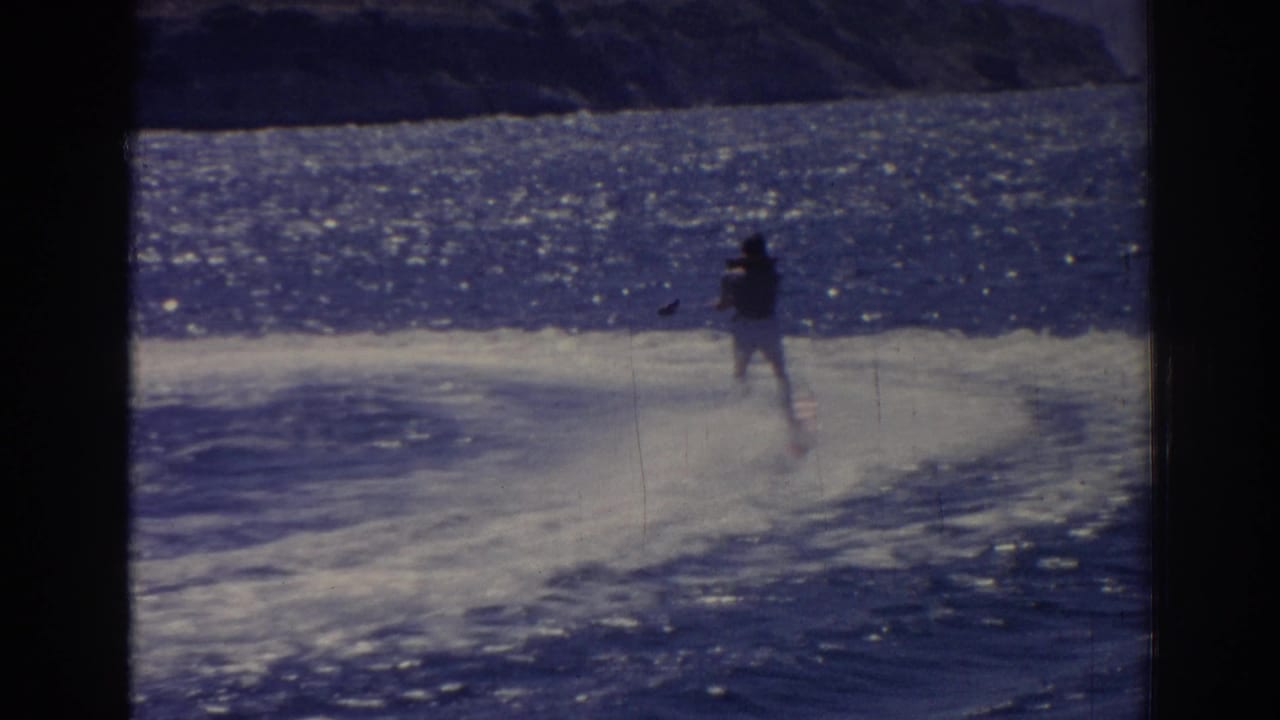 Distant water skier crossing bright blue water with a white wake behind.