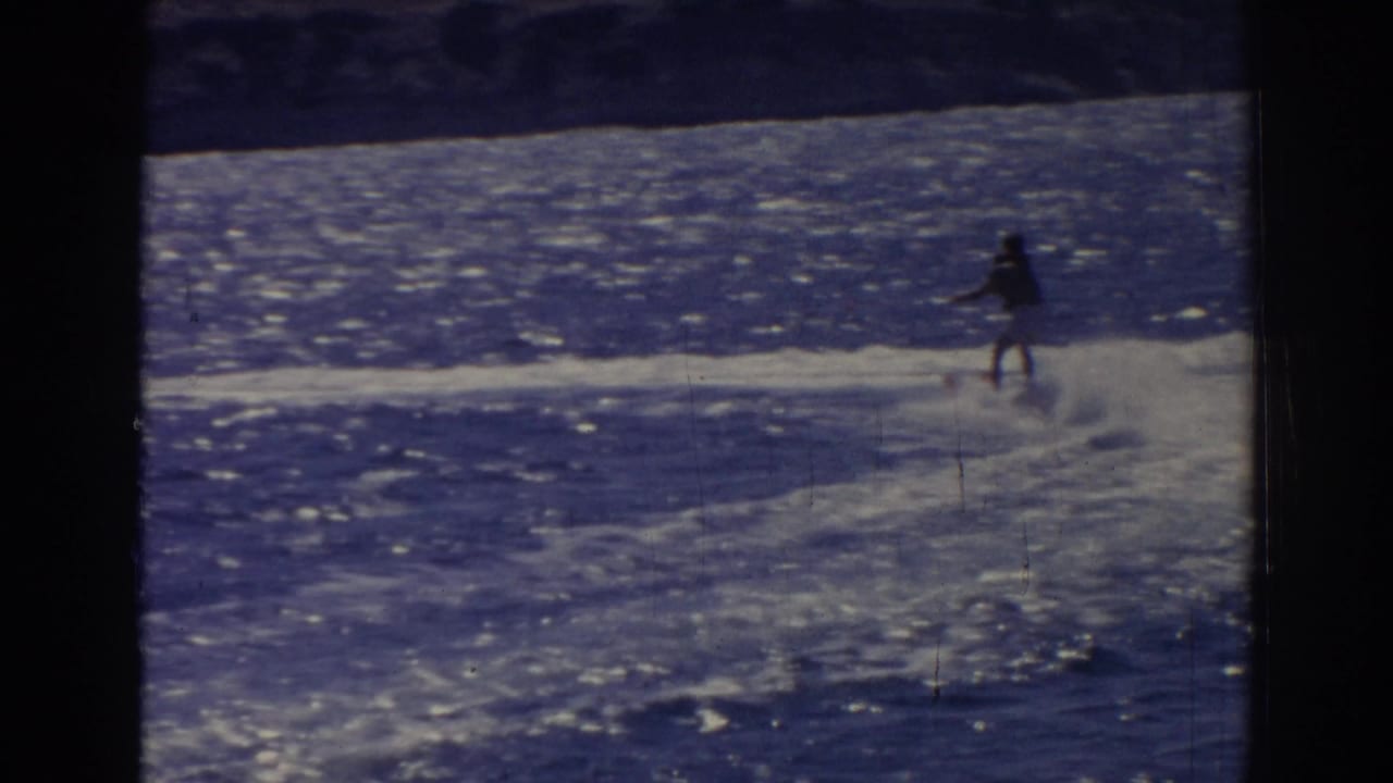 Distant 1962 Izmir water-skiing view with the skier silhouetted against bright blue water and a low shoreline.