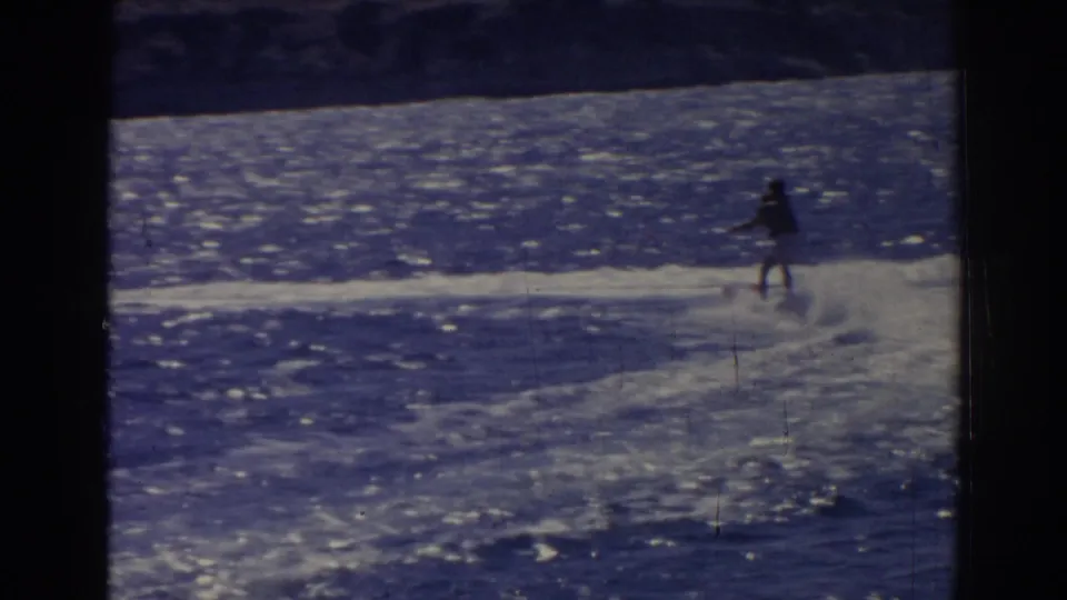 Distant 1962 Izmir water-skiing view with the skier silhouetted against bright blue water and a low shoreline.