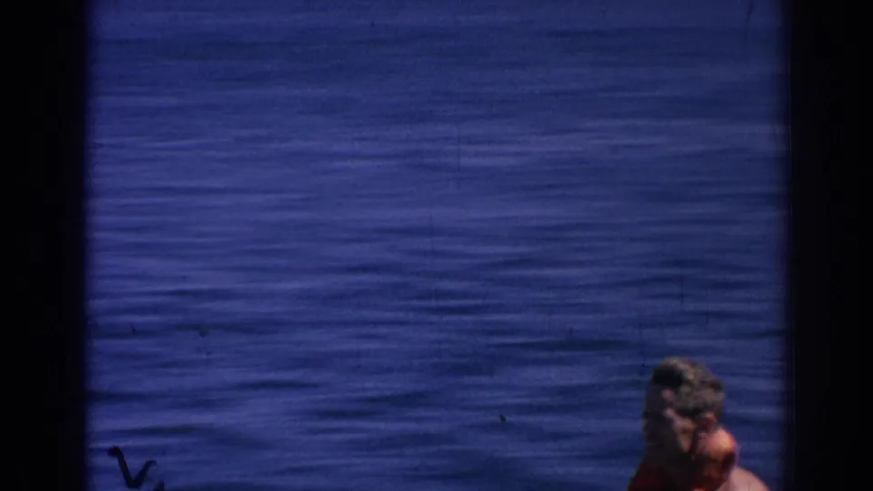 The camera catches the skier low at the bottom edge as the surrounding frame fills with blue sea and 8mm film marks.