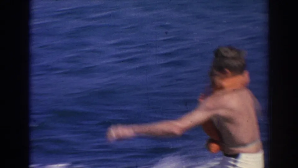 A closer, soft-focus frame shows the water skier in a life vest losing balance near the surface of the sea.