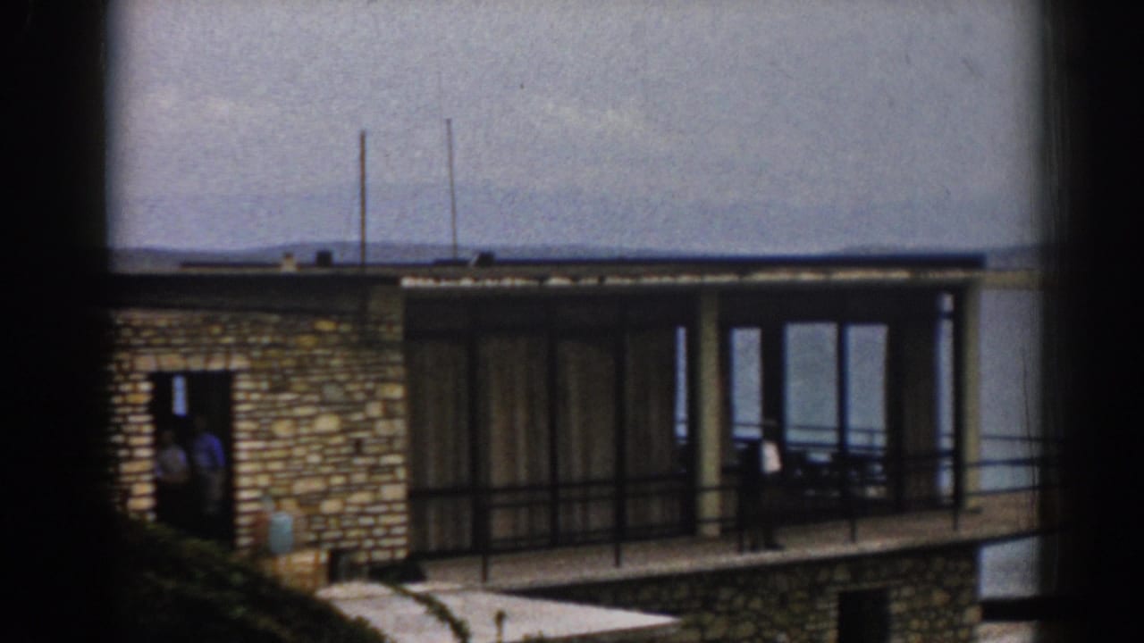 1962 Izmir frame of the same seaside residence, with stonework, large windows, balcony railings, and calm water behind it.