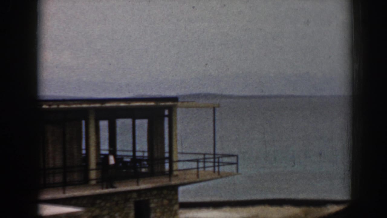 Waterfront building with large windows and balcony beside calm sea water.