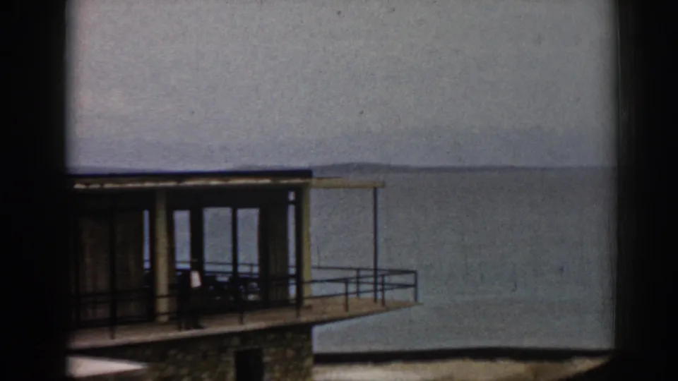 1962 Izmir home-movie frame showing a modern waterfront building with balcony railings and calm water beyond.