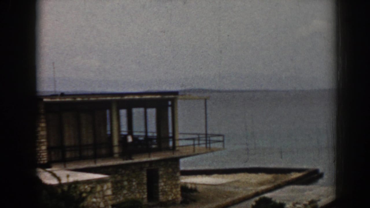 Stone waterfront building with glass doors, balcony, and sea in the background.