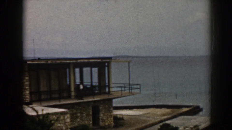 1962 Izmir coastal view with a stone-and-glass building, balcony deck, and hazy sea horizon behind it.