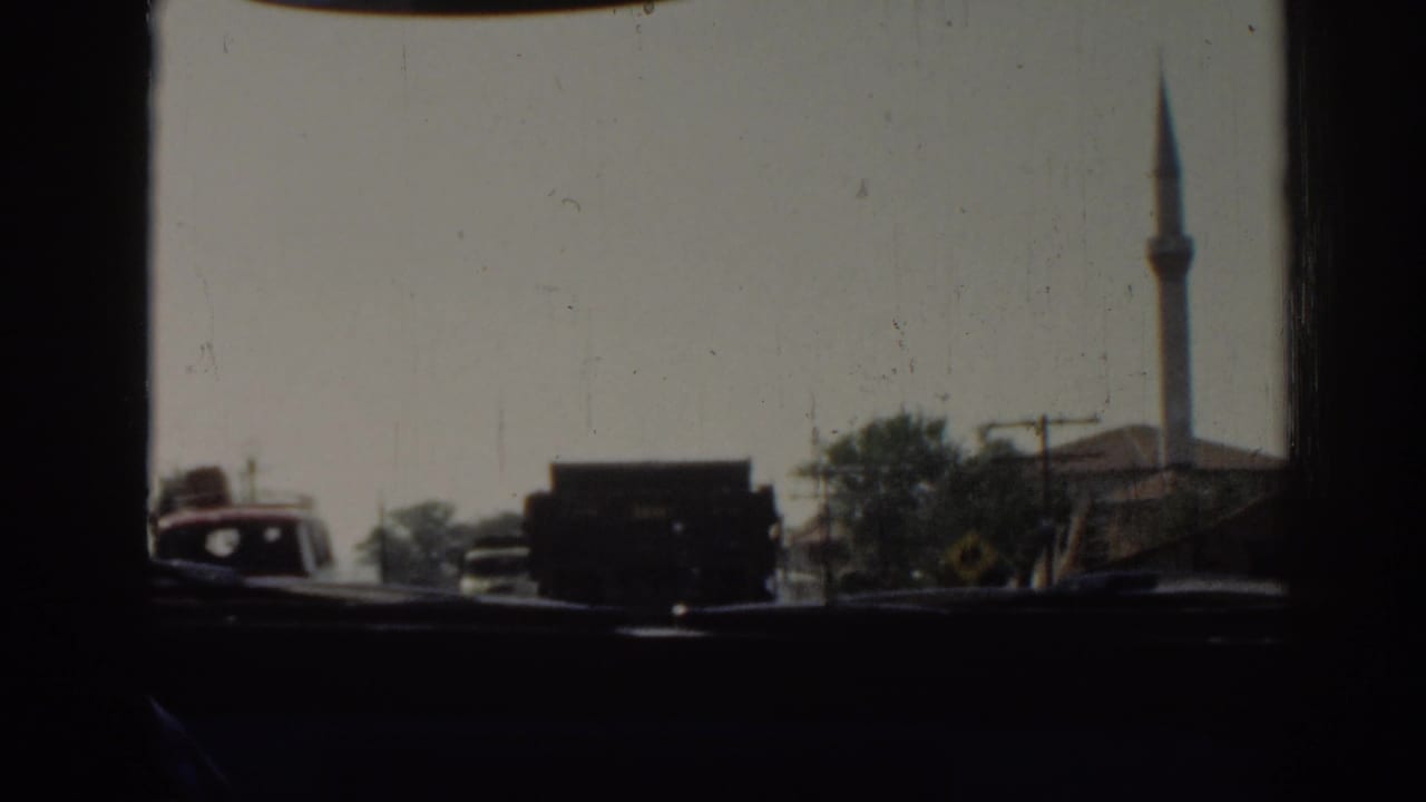 Traffic seen from inside a moving vehicle in Izmir, Turkey, with a dark truck ahead and a minaret behind roadside buildings.