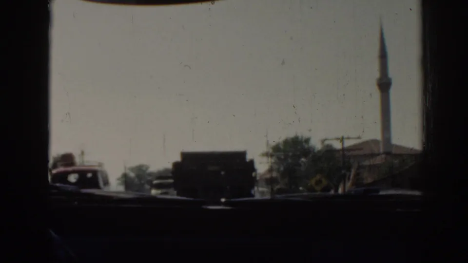 Traffic seen from inside a moving vehicle in Izmir, Turkey, with a dark truck ahead and a minaret behind roadside buildings.