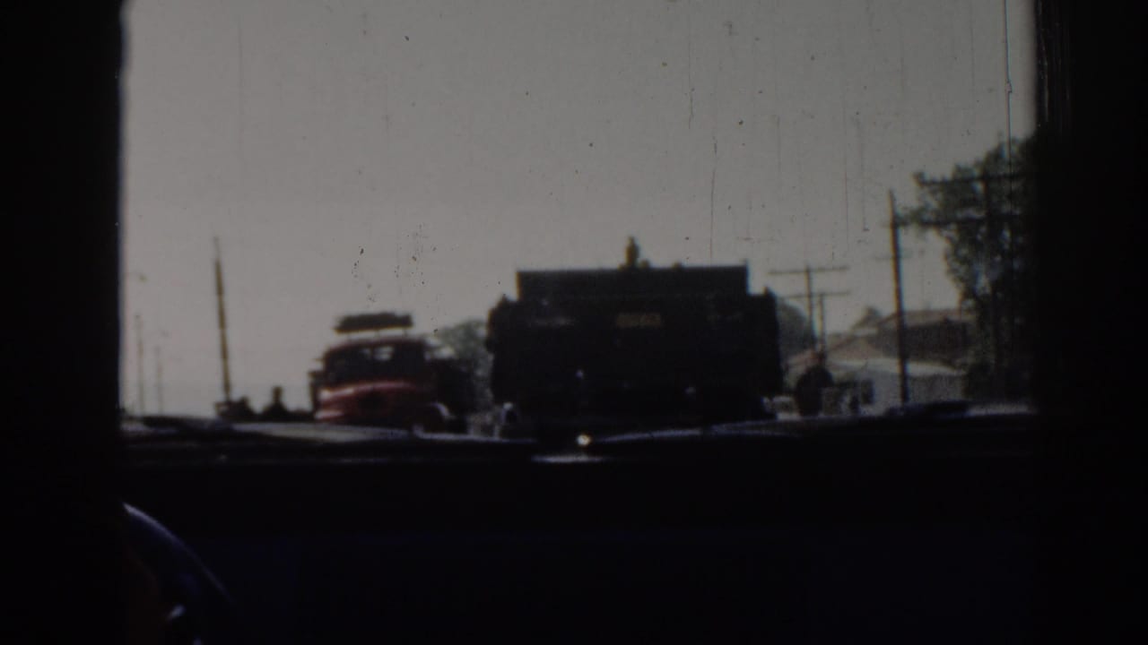View through a car windshield toward a red truck and dark truck on a sunny road.