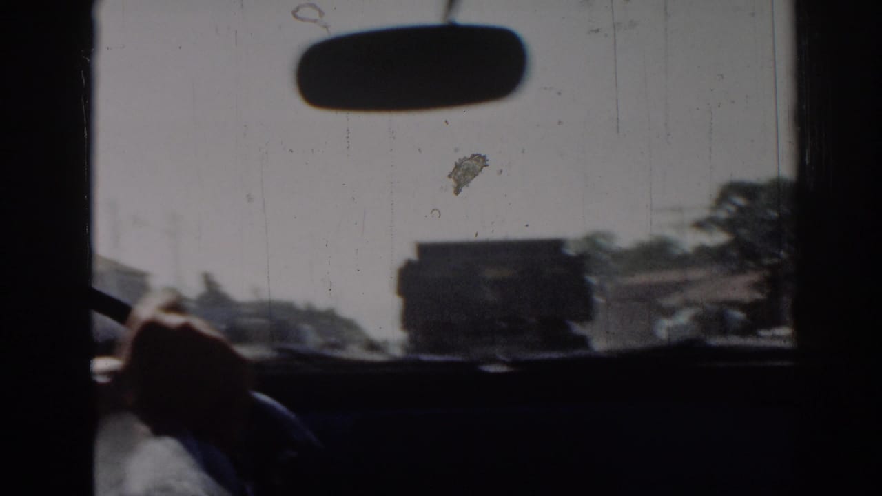 1962 Izmir driving view through a windshield, showing a rearview mirror, driver's hand, road, buildings, and a dark truck ahead.