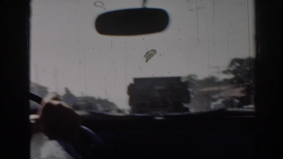 1962 Izmir driving view through a windshield, showing a rearview mirror, driver's hand, road, buildings, and a dark truck ahead.