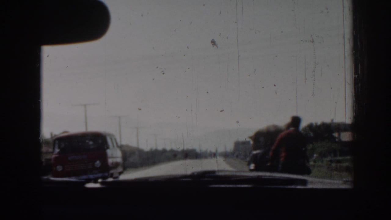 From inside the car in Izmir, a red van passes close by as a man pulling a cart moves along the roadside.