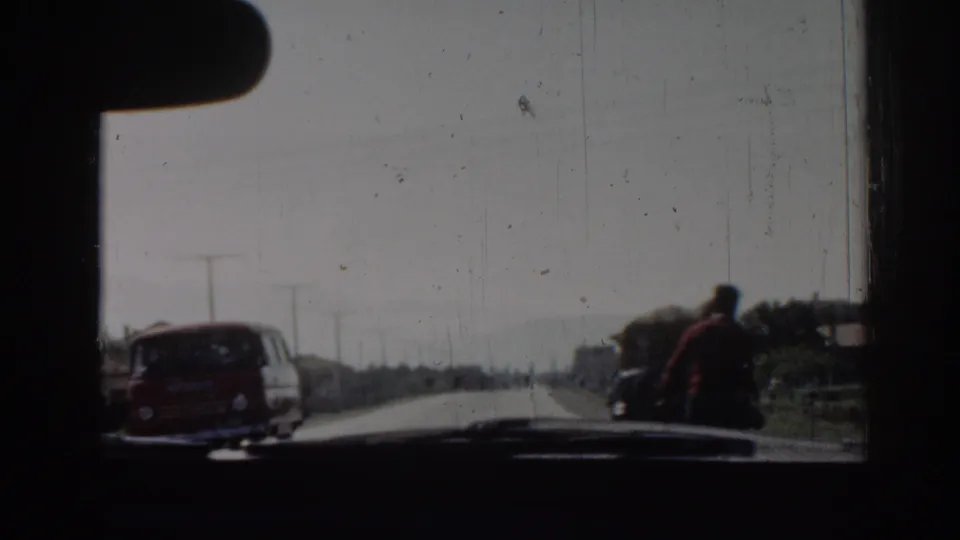 From inside the car in Izmir, a red van passes close by as a man pulling a cart moves along the roadside.
