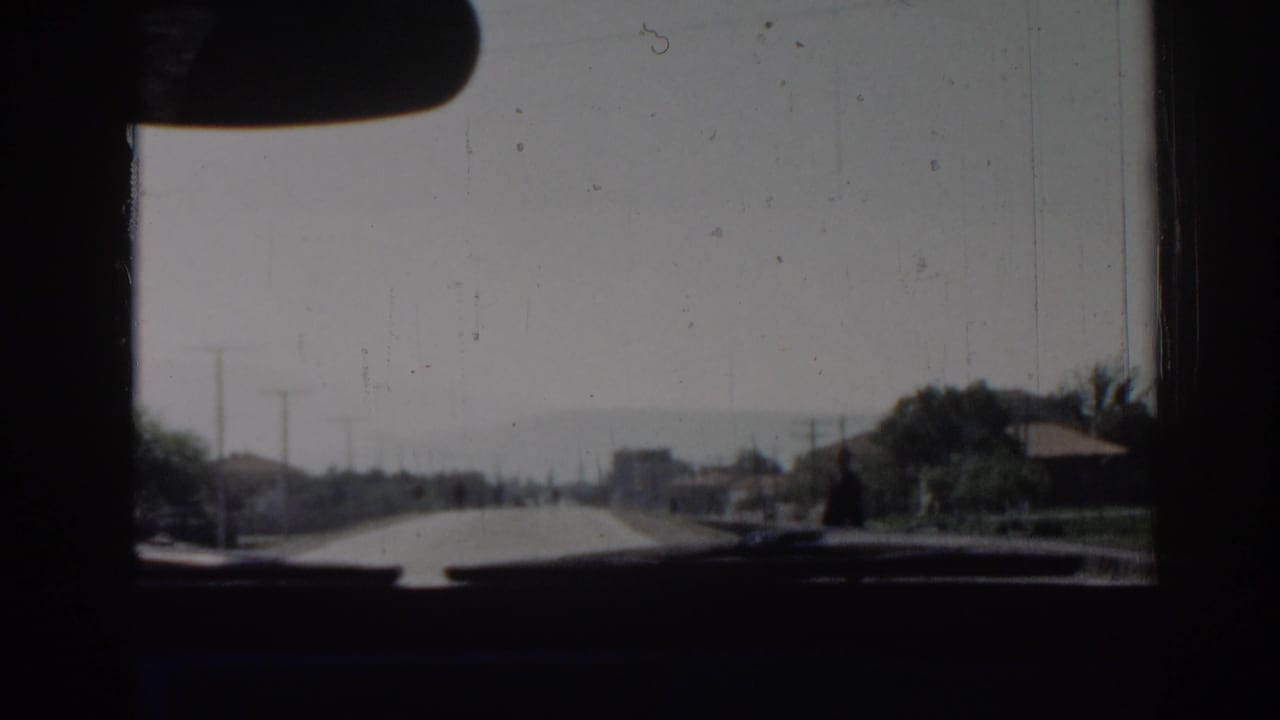 View through a car windshield toward a bright road with distant vehicles and roadside poles.