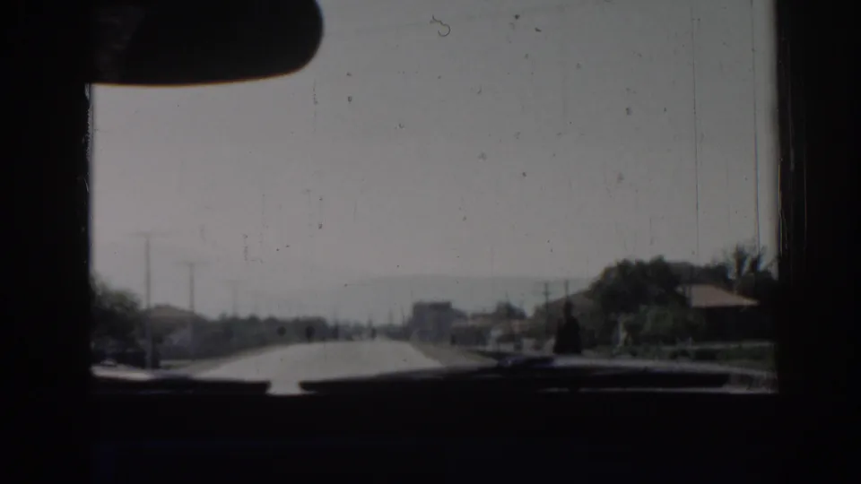 Interior car view in Izmir, Turkey, 1962, looking down a sunlit road with dashboard shadows, utility poles, and distant traffic.