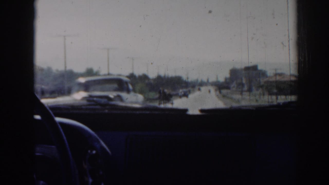 From inside a car in Izmir, Turkey, the 1962 footage shows an oncoming vehicle, distant road users, poles, trees, and dashboard shadows.