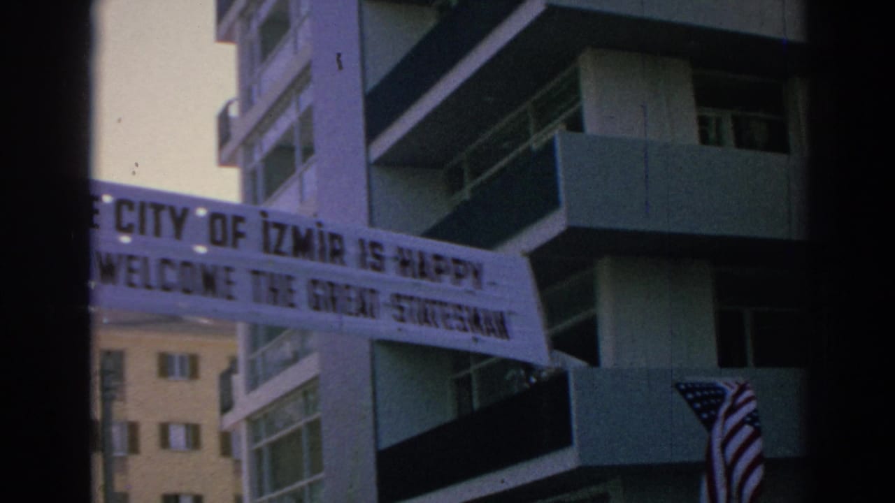 Handheld 8mm frame from Izmir showing the welcome banner crossing in front of residential-style buildings.