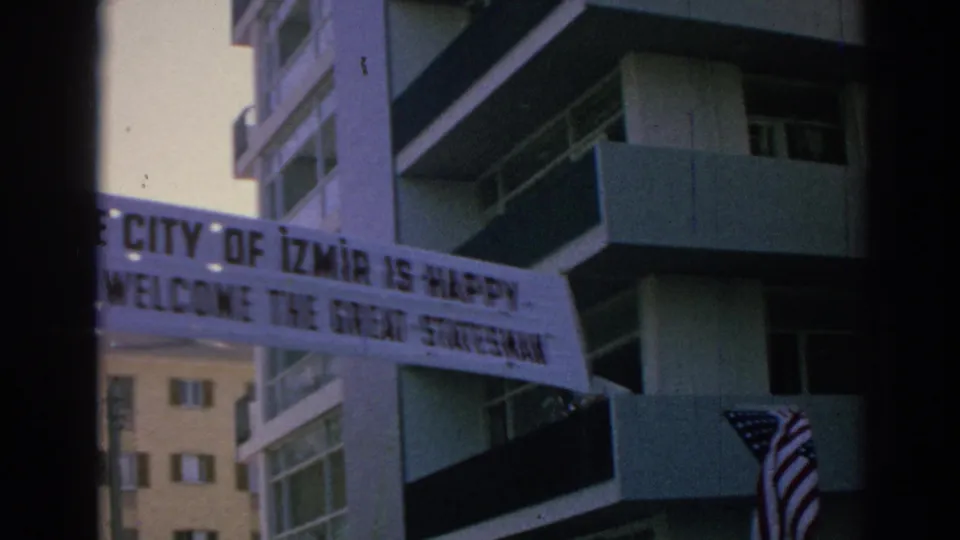 Handheld 8mm frame from Izmir showing the welcome banner crossing in front of residential-style buildings.