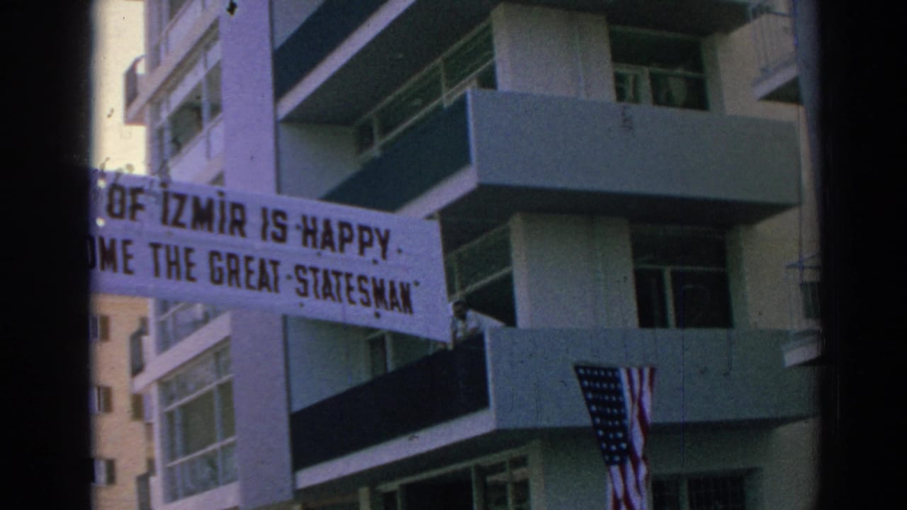 Izmir welcome banner beside apartment balconies, with Turkish and American flags visible below in the 1962 clip.