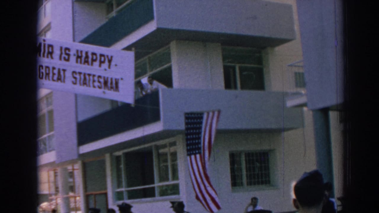 Banner and American flag hang from a building as people stand below.