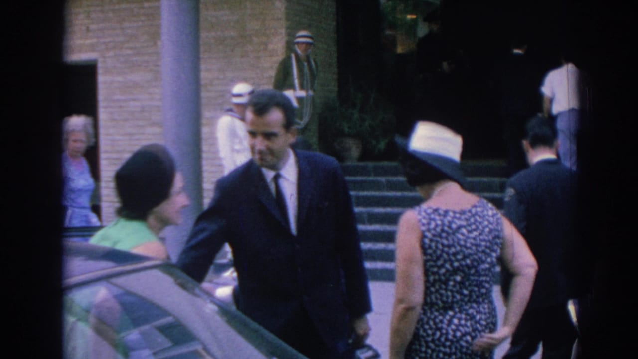 1962 Izmir arrival scene with a suited man, a woman in green, a woman in a patterned dress and hat, a car, and a doorman at the entrance.