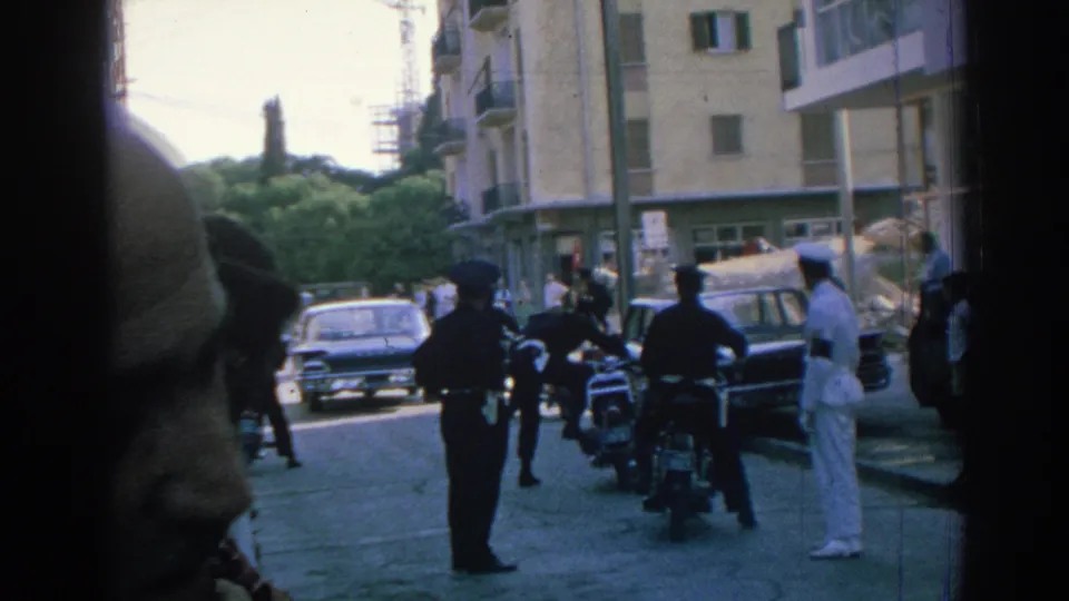 1962 Izmir street scene with police near motorcycles, a sailor in white, parked cars, and a close foreground pedestrian.