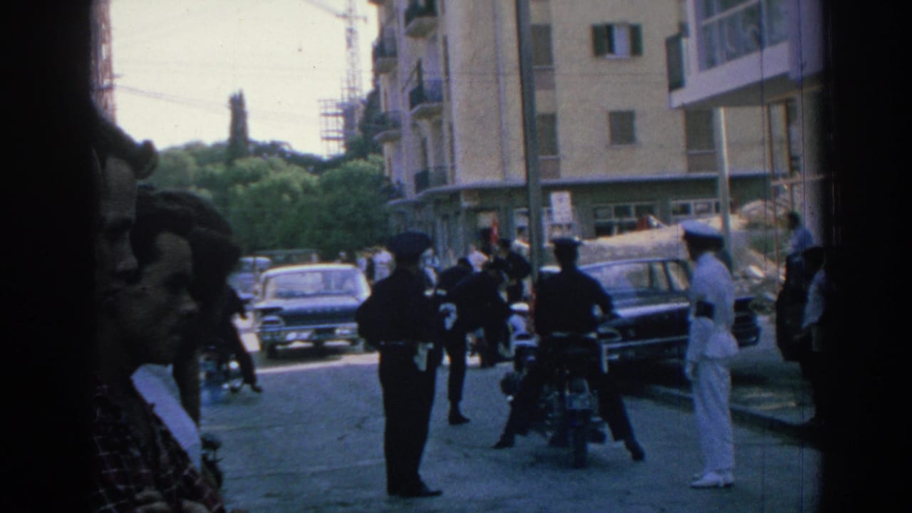 1962 Izmir street view with officers beside motorcycles, a sailor at right, parked cars, pedestrians, apartment buildings, and greenery.