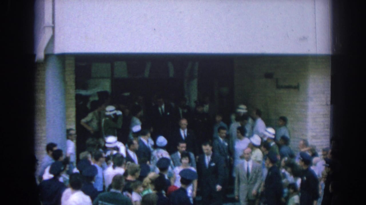 A 1962 Izmir crowd fills a building entrance area as officers, suited men, and onlookers gather around the doorway.