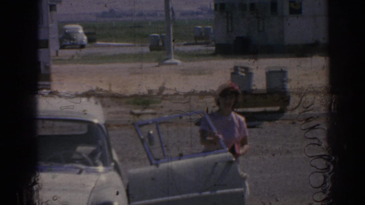 Woman standing beside a white car with an open door at an airfield.