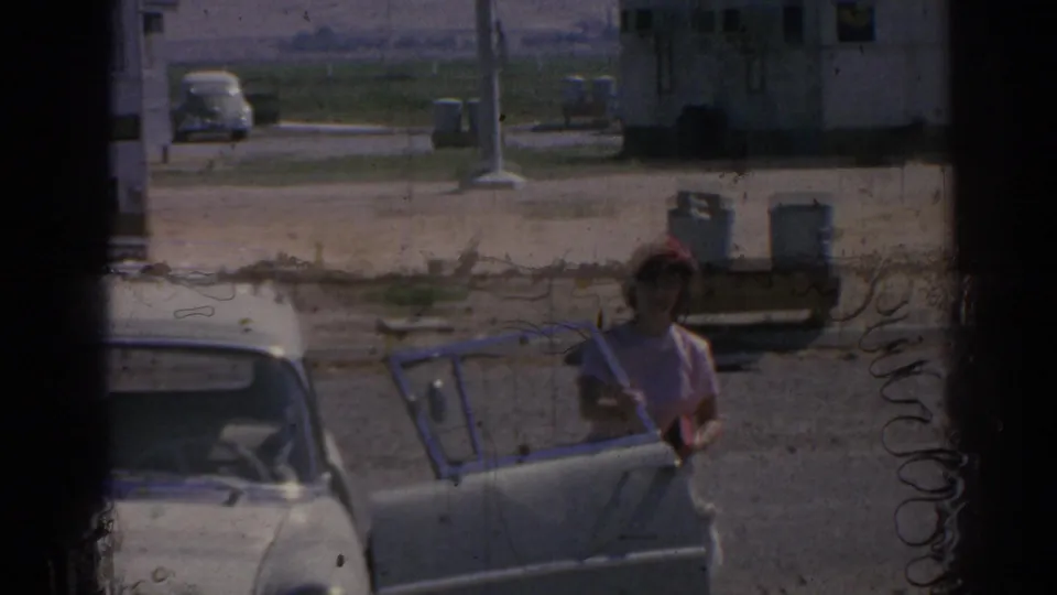 In 1962 Izmir, Turkey home-movie footage, a woman in a red headscarf stands beside a white car near an airfield.