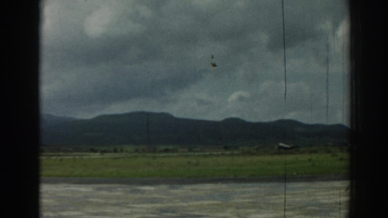 The 1962 Izmir airfield view shows a small aircraft low on the runway area, with grass, mountains, and cloudy sky behind it.