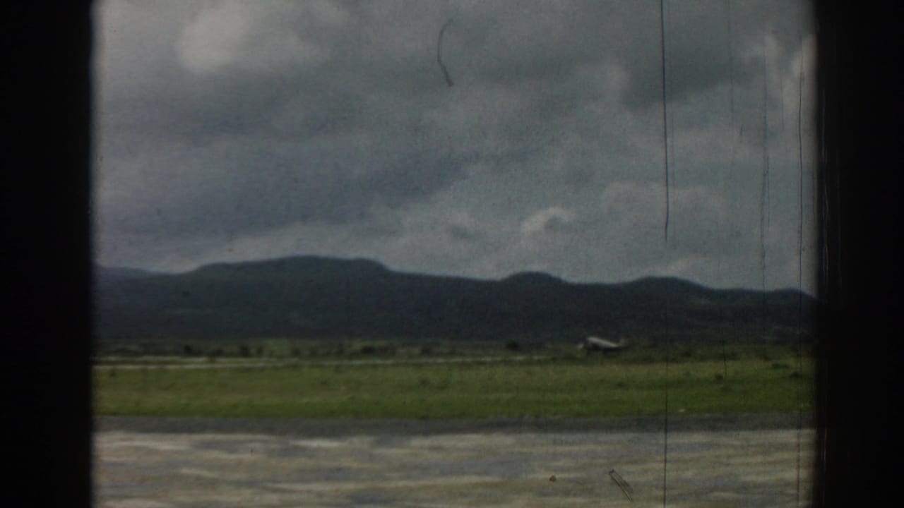 Small airplane on a grassy airfield below dark mountains and cloudy sky.