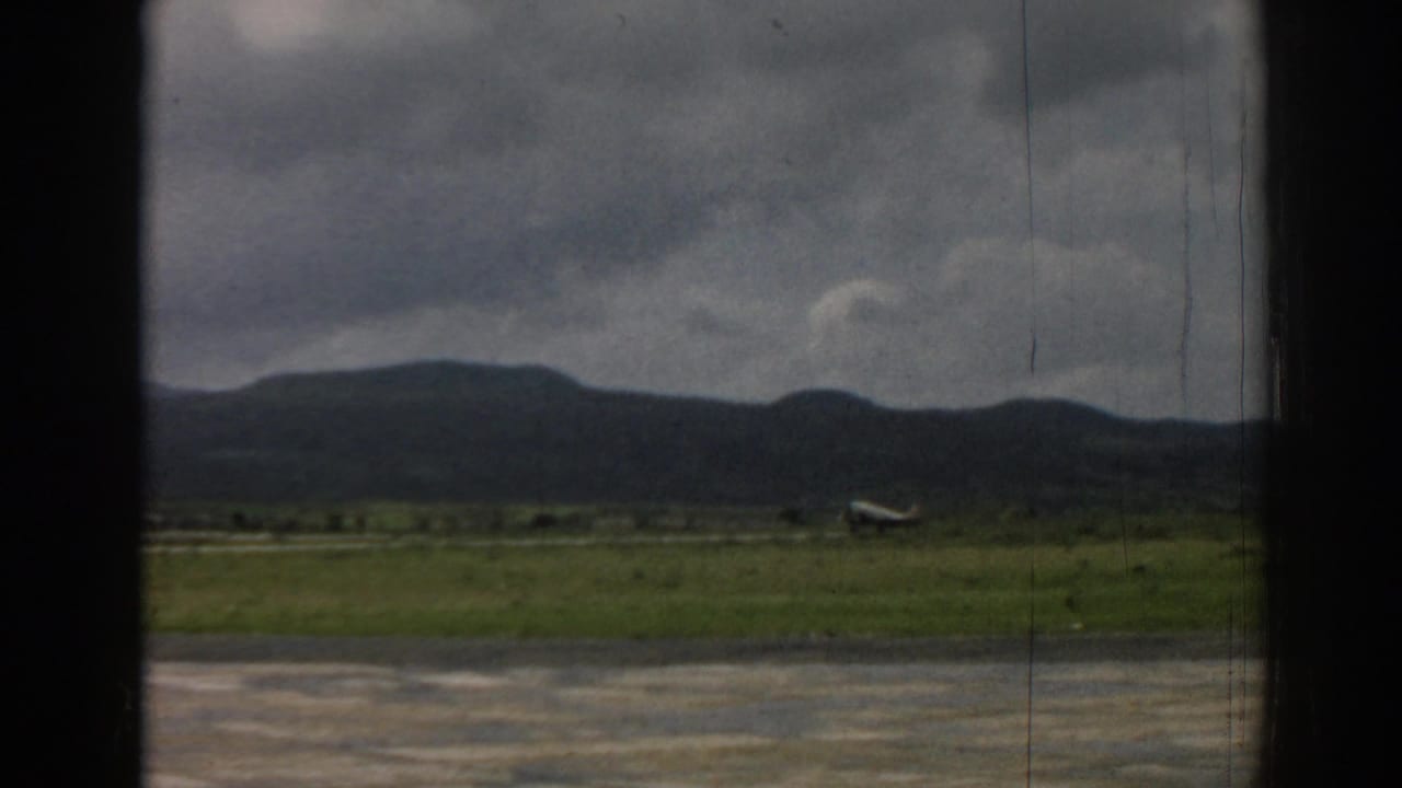 1962 Izmir 8mm frame of a small aircraft progressing along a grassy airfield beneath a heavy cloud cover.