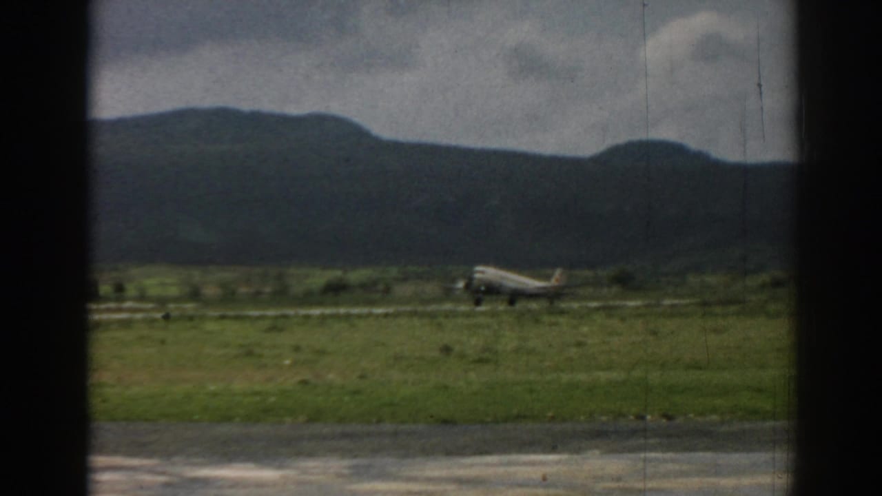 Silver aircraft on a grassy airfield seen through dark window framing.