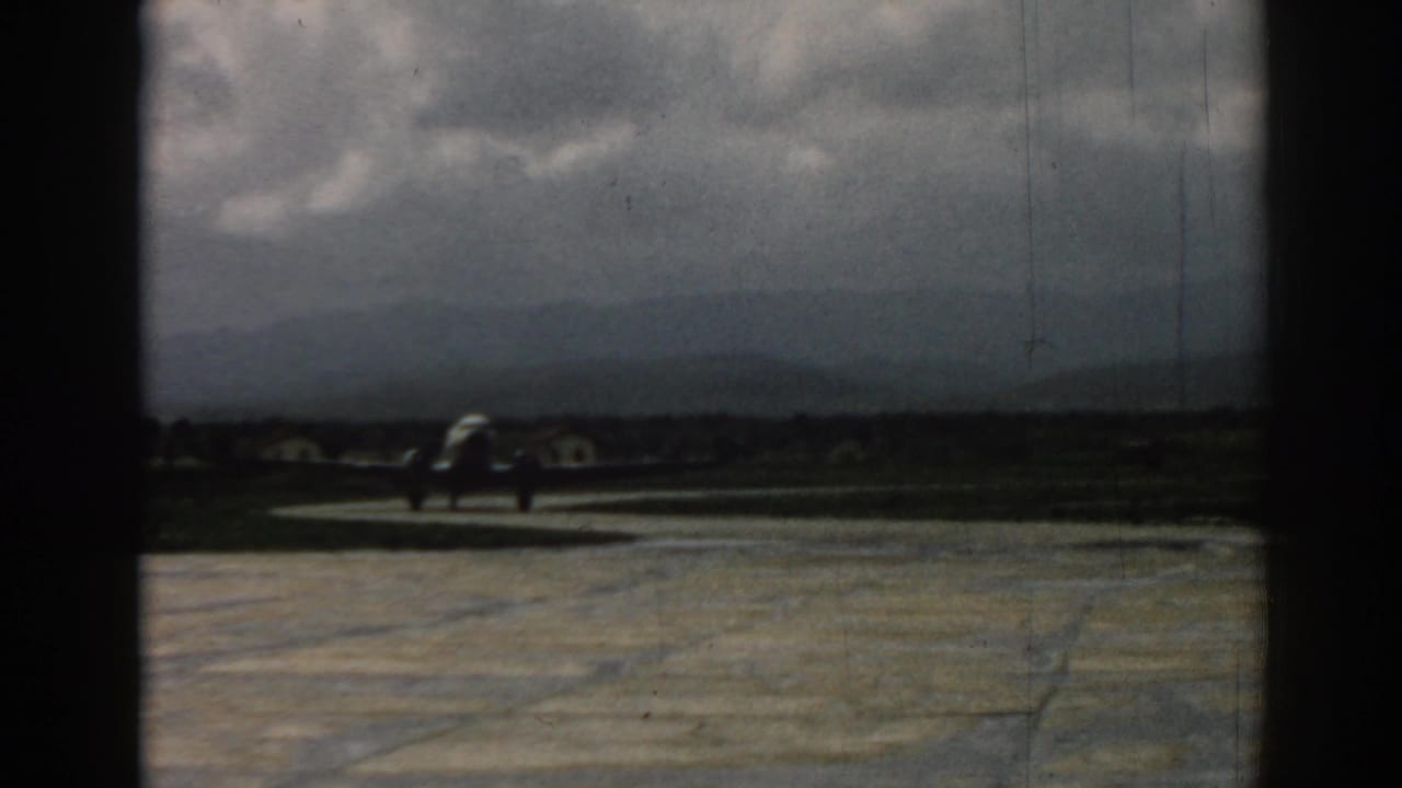 The aircraft continues along the runway at Izmir, seen through the home-movie camera's dark framing and aged color.