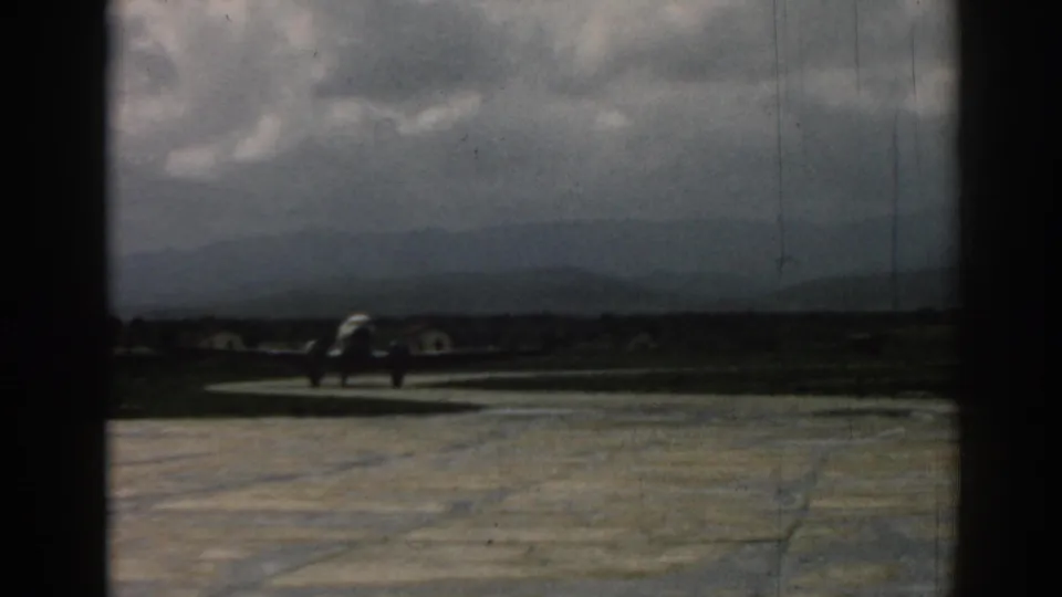The aircraft continues along the runway at Izmir, seen through the home-movie camera's dark framing and aged color.
