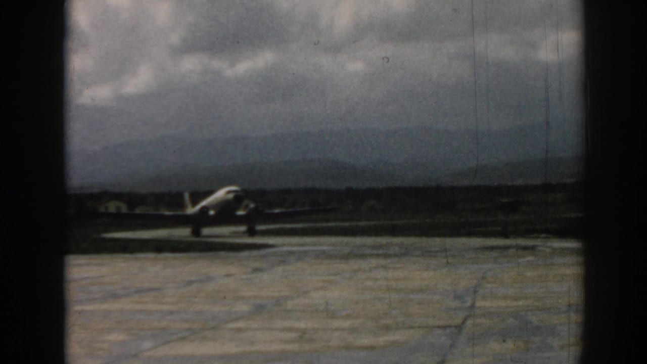 Propeller airplane on a tarmac under a cloudy sky with distant hills.