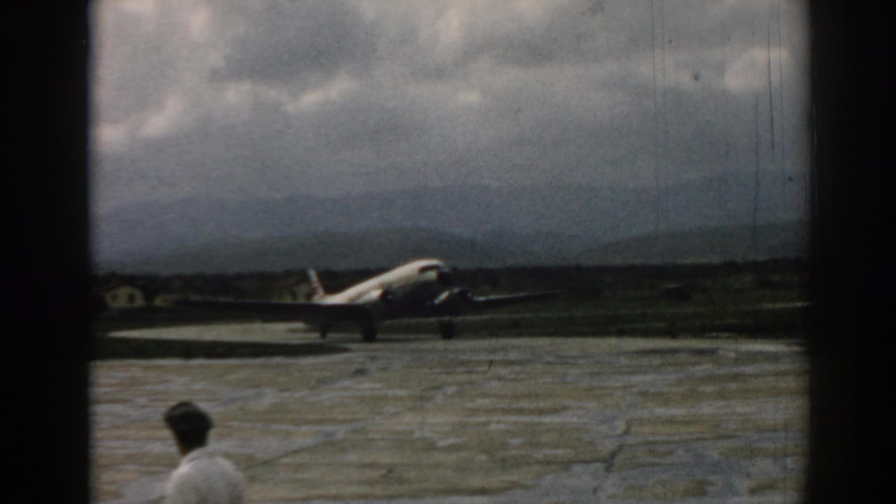 1962 Izmir tarmac view with a man walking across the foreground and a propeller airplane behind him.