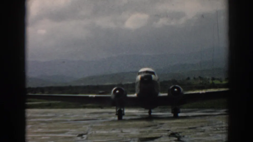 Late frame of the 1962 Izmir clip with the propeller aircraft closer on the tarmac, hills and gray clouds still visible behind it.