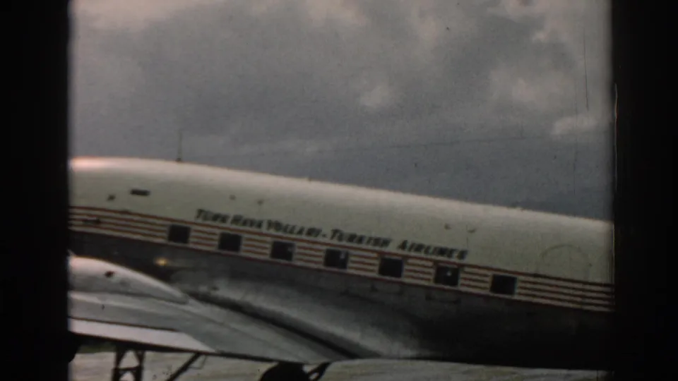 In the Izmir 1962 home-movie frame, the Turkish Airlines fuselage passes behind a dark vertical frame with windows and wing visible.