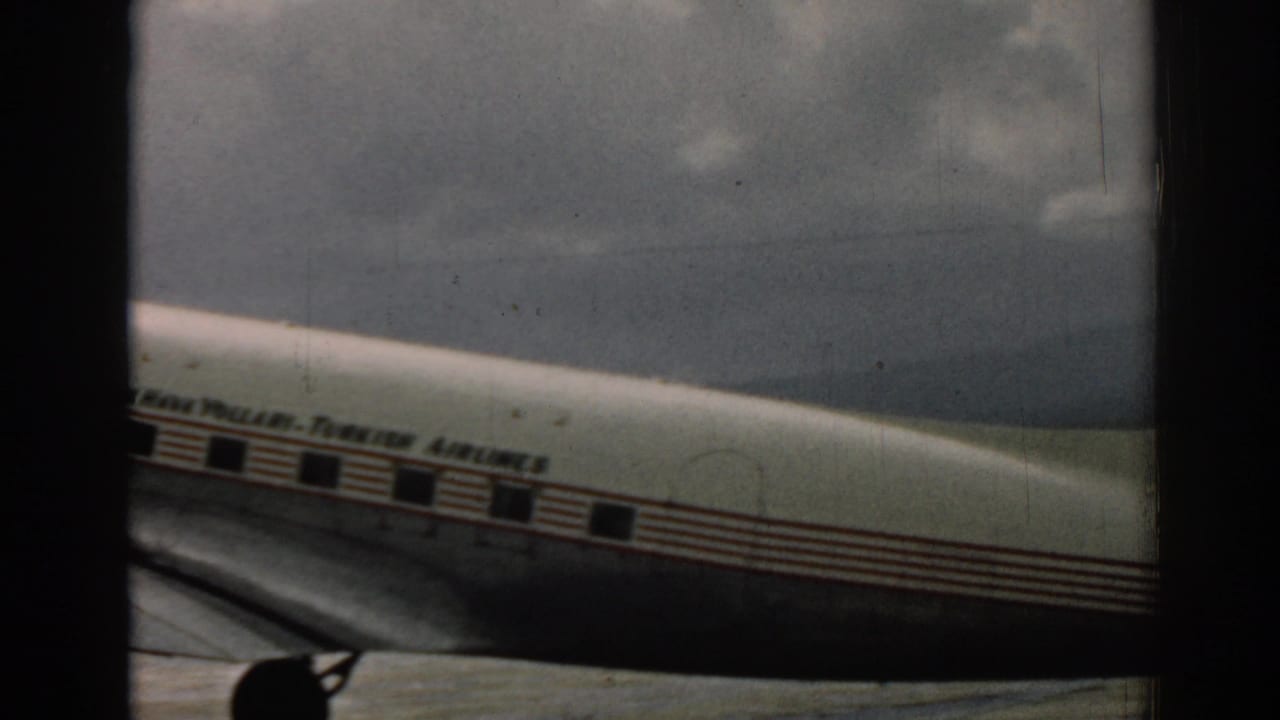 1962 Izmir airport footage shows the aircraft midsection moving past, with airline lettering, red stripes, wing, and landing gear in view.