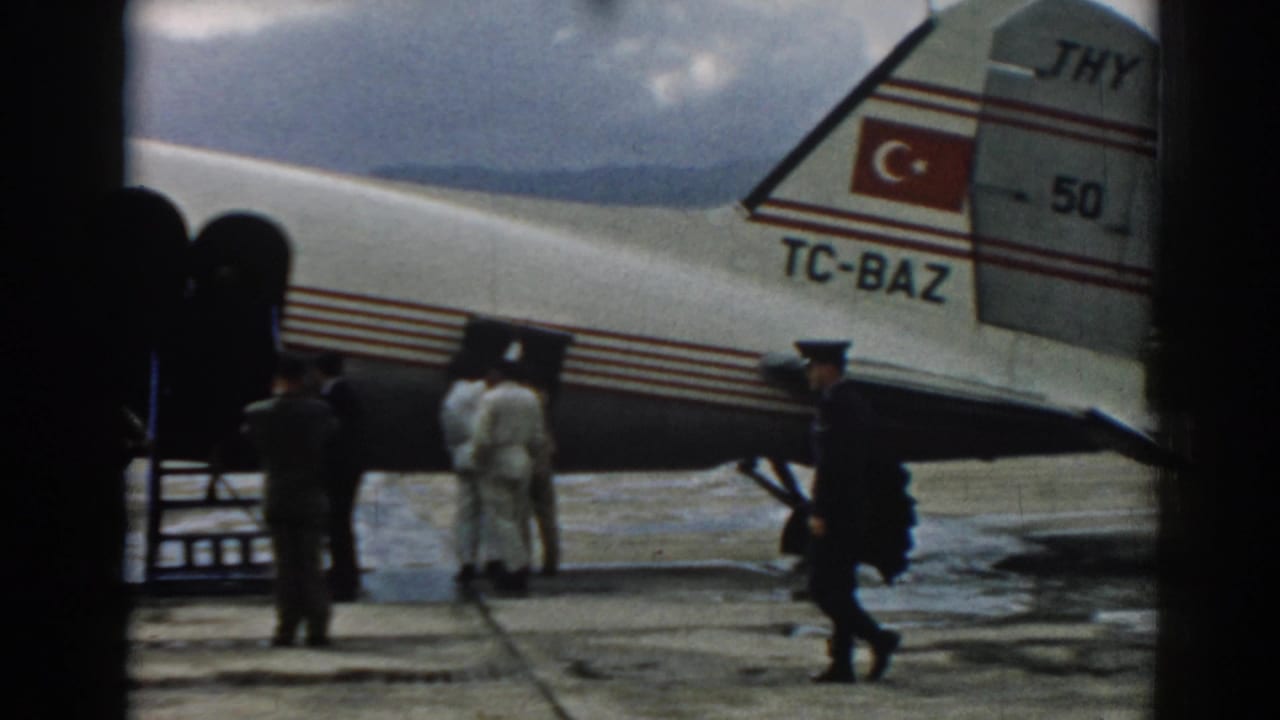 Passengers and uniformed figures stand beside a portable stairway at the aircraft door.