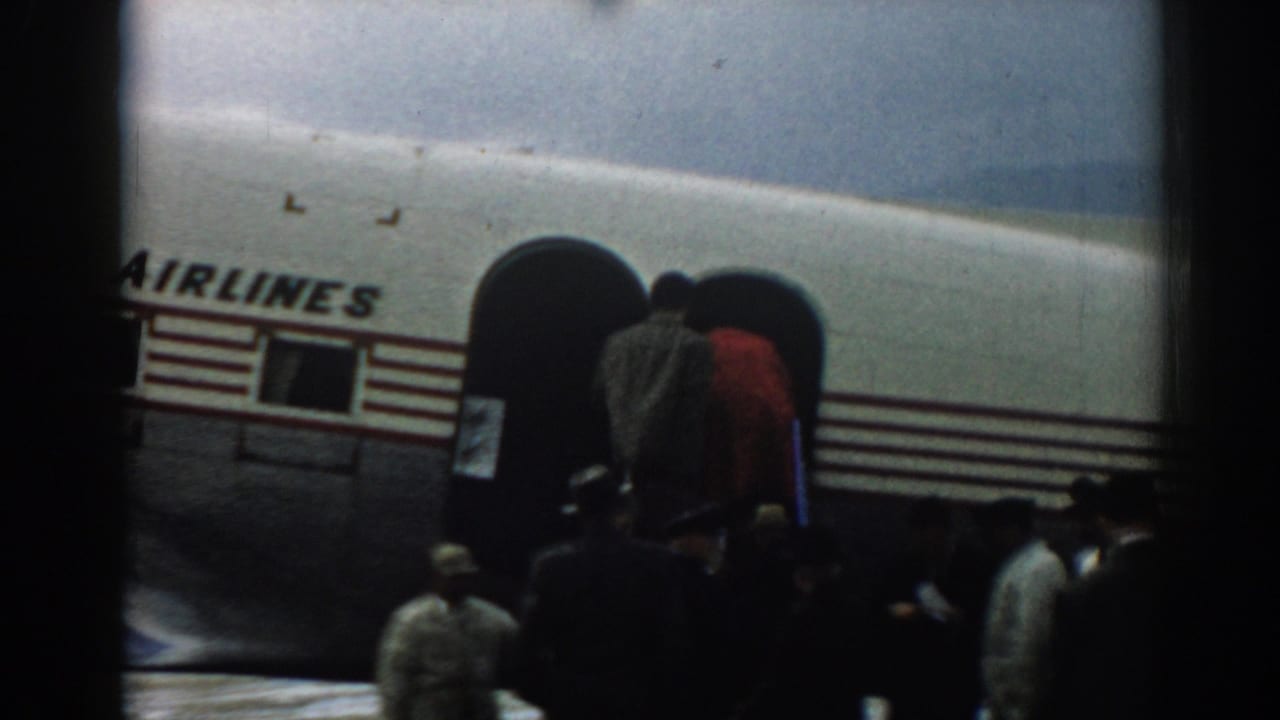 A handheld 1962 airport view shows people below the boarding stairs beside a Turkish Airlines aircraft in Izmir.