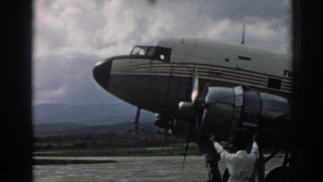 1962 Izmir frame of a Turkish Airlines propeller plane, showing the nose, engine nacelle, landing gear, cloudy sky, and directing crew member.
