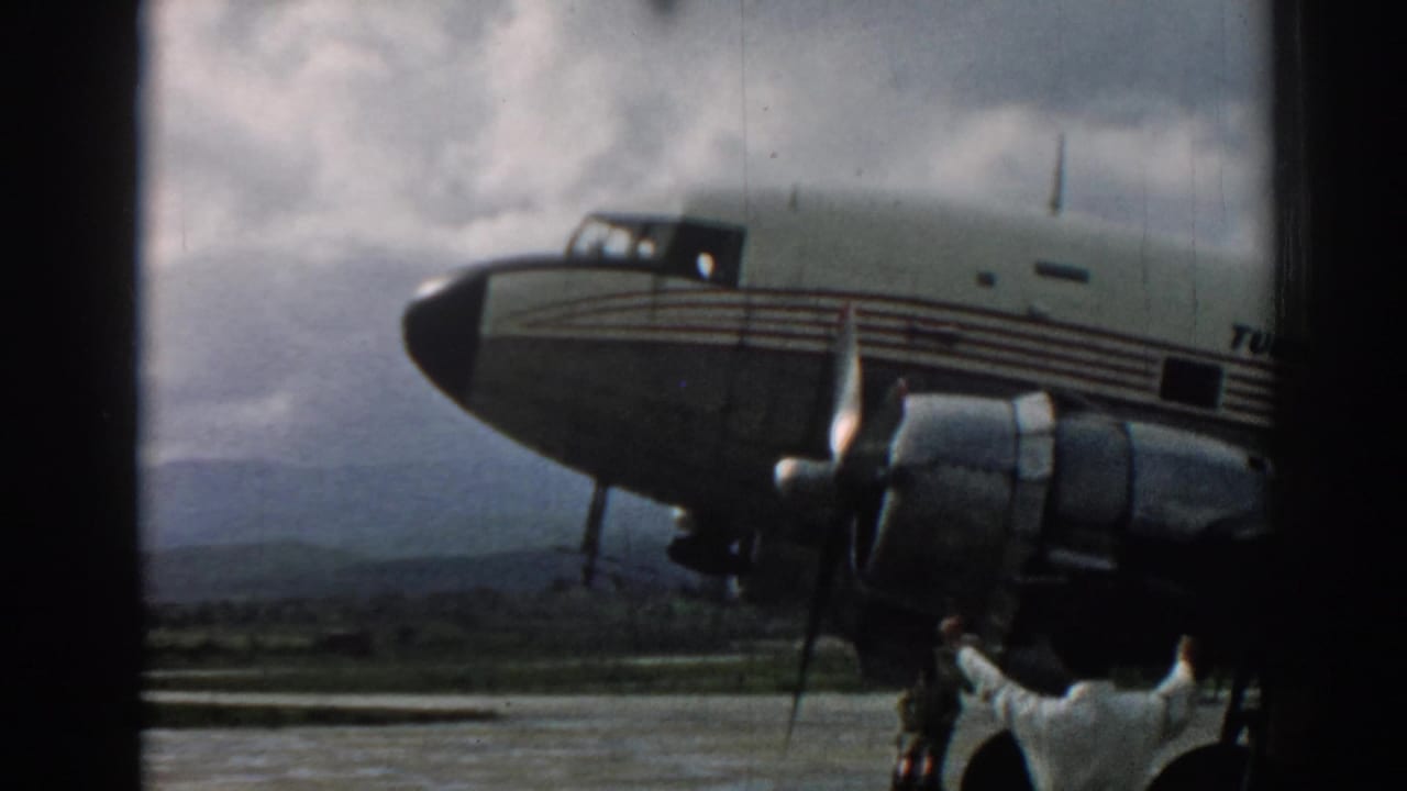 Vintage 8mm view from Izmir in 1962 showing crew beside a propeller aircraft against cloudy hills.
