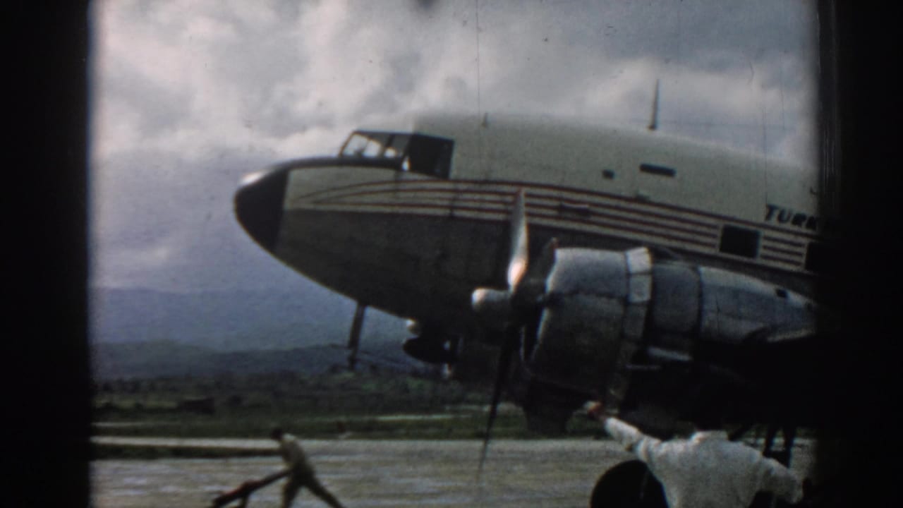 Vintage propeller aircraft nose on a tarmac with ground crew near the engine.